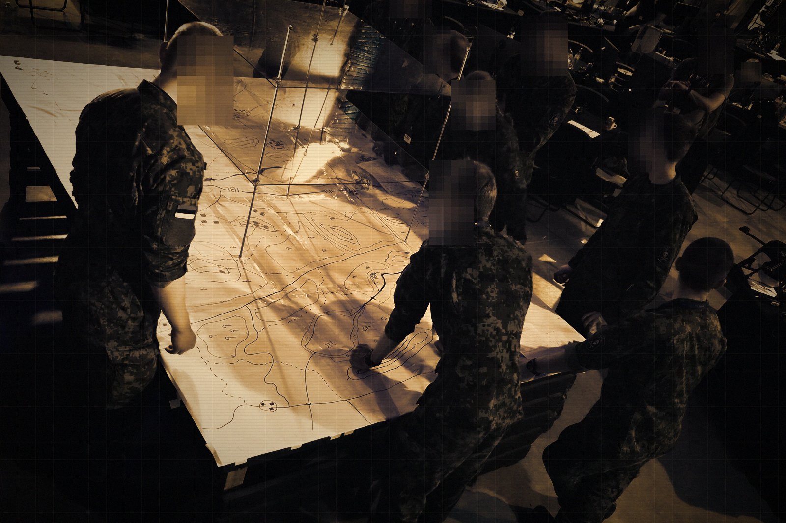 A team standing around a paper map table during a tabletop wargame, with acrylic altitude layers above the map surface. Faces are obscured.